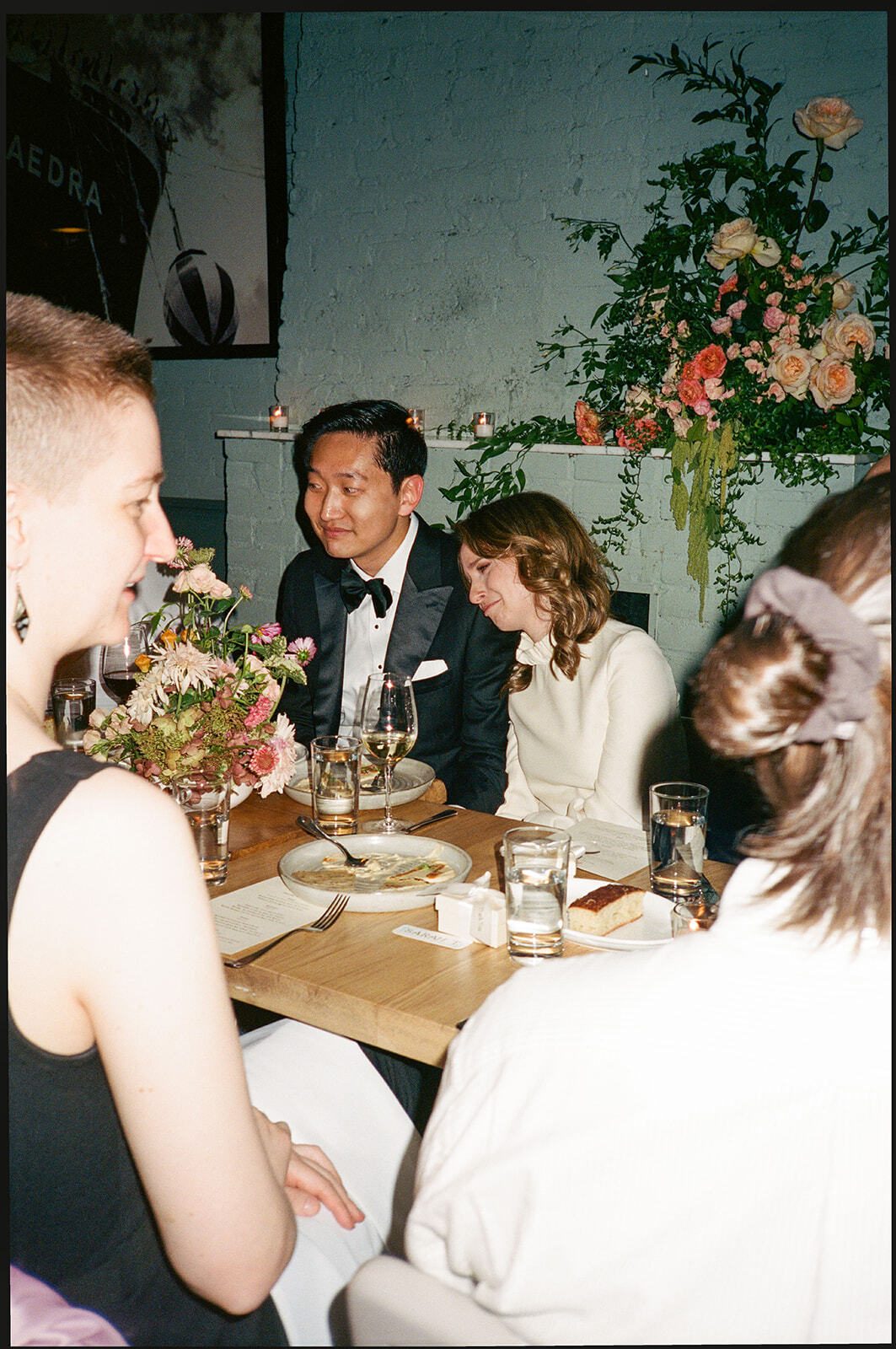 Guests in black tie seated at the wedding dinner table under a floral arrangement, Adena and Brian's wedding, by Brooklyn wedding photographer Lana Dubkova on film.